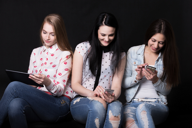 Group of beautiful girlfriends using different devices, sitting together but paying attention only to their mobile phones and tablet, best friends having fun
